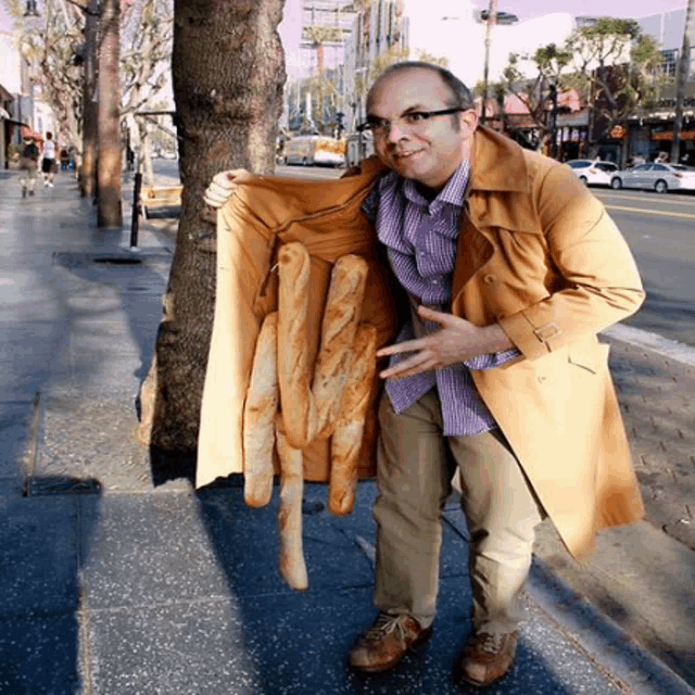 a man in a trench coat is holding a bunch of bread sticks