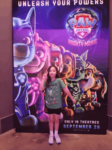 a girl poses in front of a paw patrol movie poster