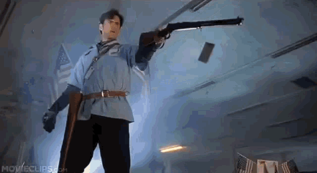a man in a blue shirt is holding a shotgun and throwing a piece of paper in the air .