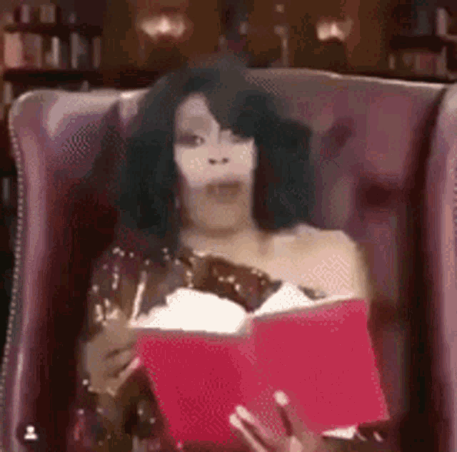 a woman is sitting in a chair holding a pink book .
