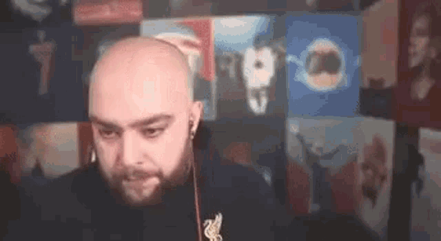 a bald man with a beard wearing headphones is sitting in front of a wall with pictures on it .