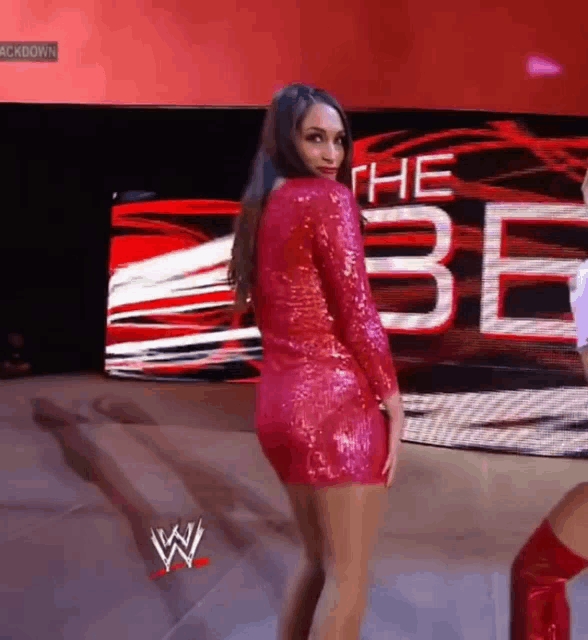 a woman in a red sequined dress is standing in front of a sign that says " the be "