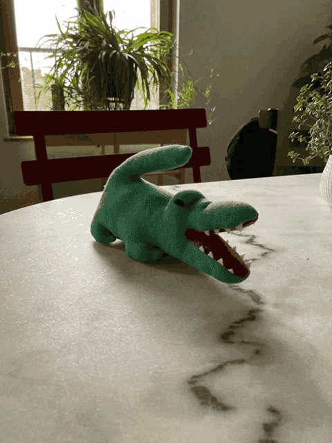 a stuffed crocodile is laying on a table in front of a window