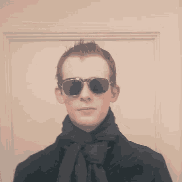 a young man wearing sunglasses and a scarf looks at the camera