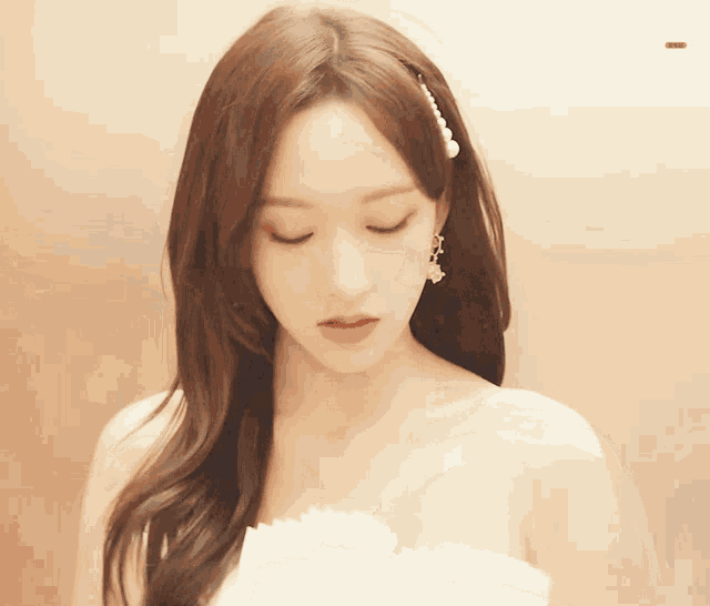 a woman in a white dress with pearls in her hair looks down