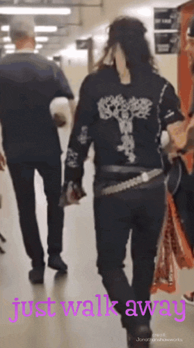 a woman in a black shirt with a cross on the back walks away from a man in a grey shirt