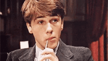 a young man in a suit is holding a pen to his mouth and looking at the camera .
