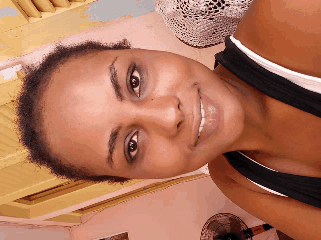 a close up of a woman 's face with a fan on the wall behind her