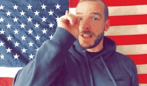 a man in front of an american flag holds up his finger