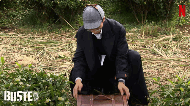 a man in a suit and hat is kneeling down with a suitcase in front of a sign that says buste