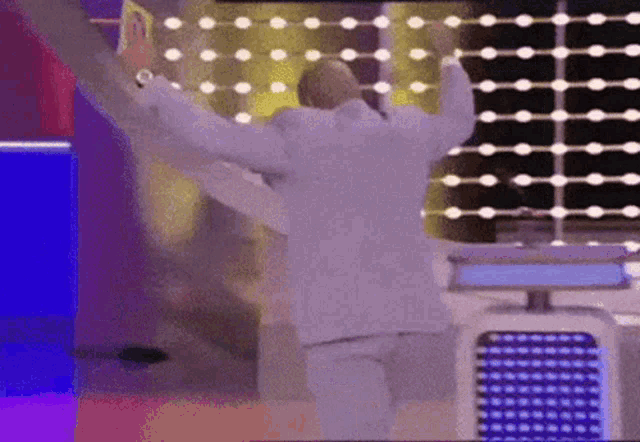 a man in a white suit is dancing on a stage with his arms outstretched