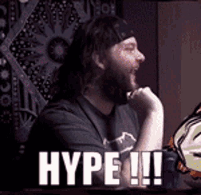 a man with a bandana on his head is sitting in front of a wall tapestry with the words hype !!! on it .