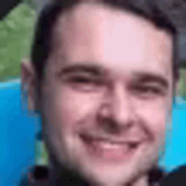 a close up of a man 's face smiling in front of a blue pool .