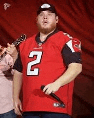 a man in a red football jersey is singing into a microphone on a stage .