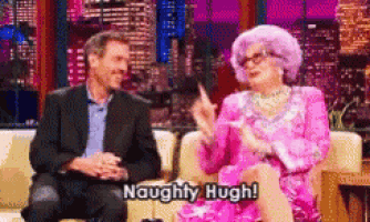 a man in a suit sits next to a woman in a pink dress who says naughty hugh .