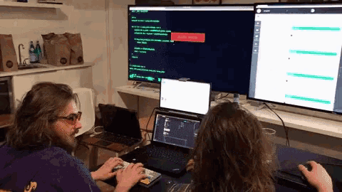 a man in a purple hoodie is typing on a keyboard in front of a computer monitor