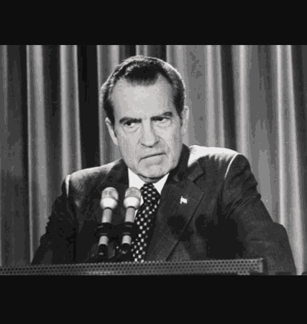 a man in a suit and tie is speaking into a microphone