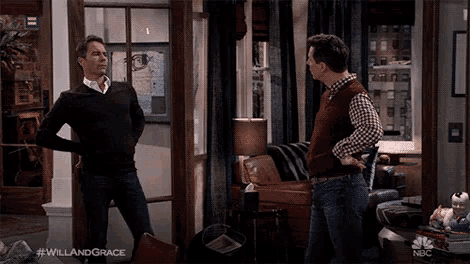 two men standing in a living room with #willandgrace on the bottom right