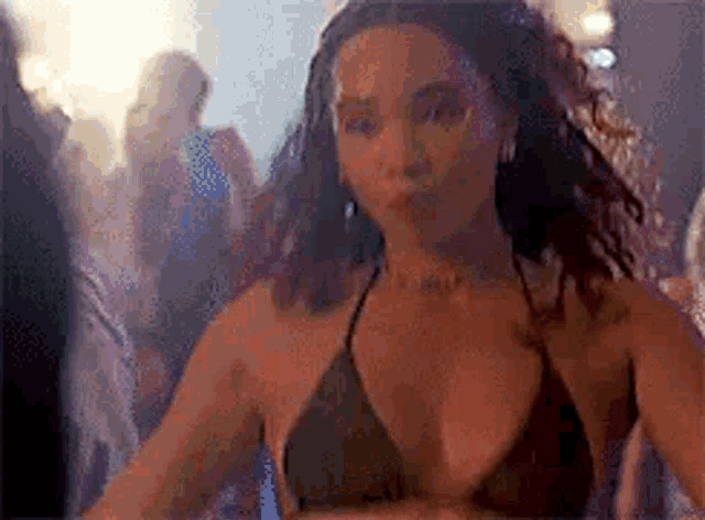 a woman in a bikini top is dancing in a club with other people .