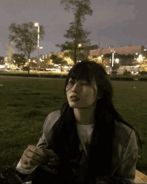 a woman is sitting in the grass with her eyes closed at night