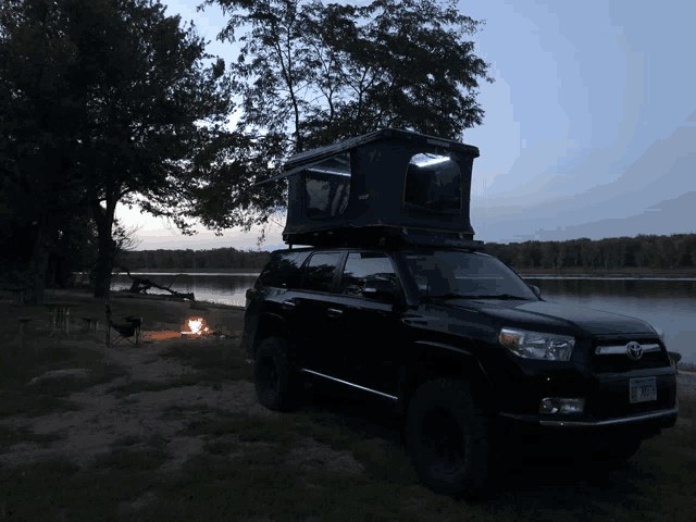 a black suv with a tent on top is parked by a lake