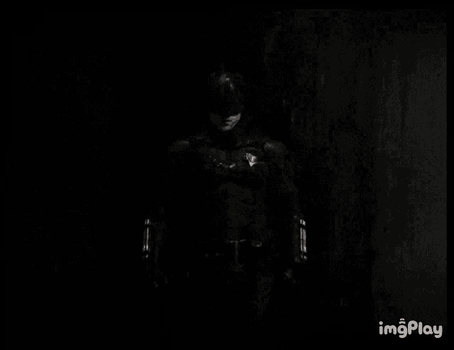 a black and white photo of a man in a batman costume standing in the dark .