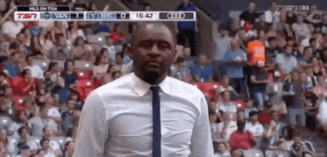 a man in a white shirt and tie is standing in front of a crowd of people in a stadium .