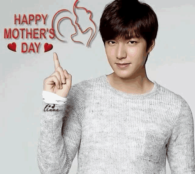 a man in a sweater is pointing up with his finger in front of a happy mother 's day sign .