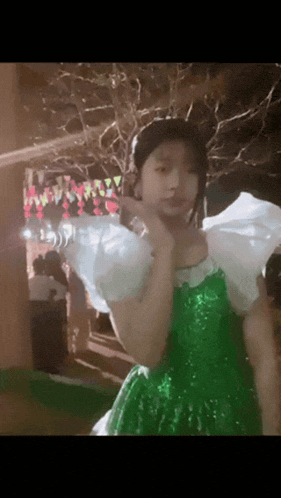 a girl in a green dress with white sleeves is standing in front of a crowd