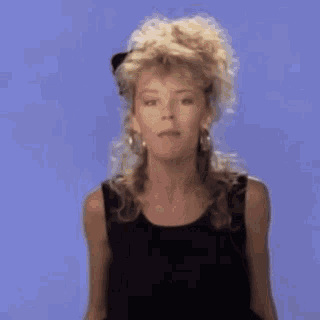 a woman in a black tank top and earrings is standing in front of a blue wall .