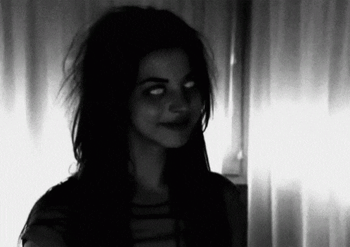 a black and white photo of a woman with white eyes looking at the camera .