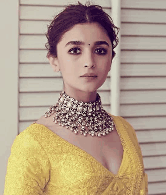 a woman is wearing a yellow blouse and a choker necklace .