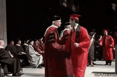 a man in a red graduation cap and gown is shaking hands with a man in a black robe .