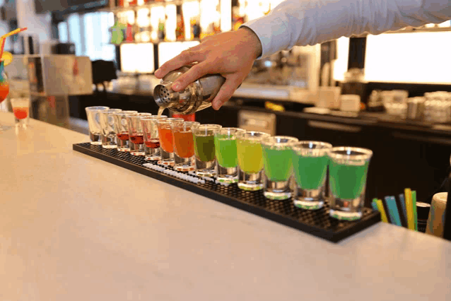 a bartender pours a drink into shot glasses
