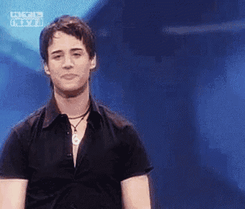 a man wearing a black shirt and a necklace is standing in front of a blue screen .