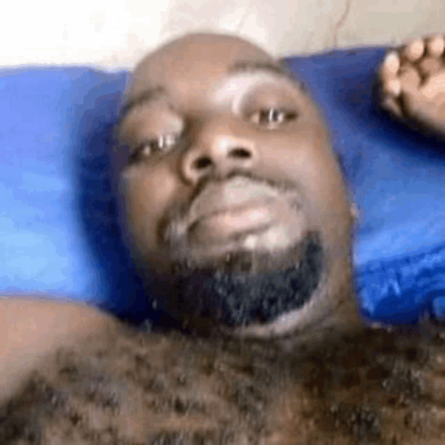 a man with a beard is laying in bed with a blue pillow .