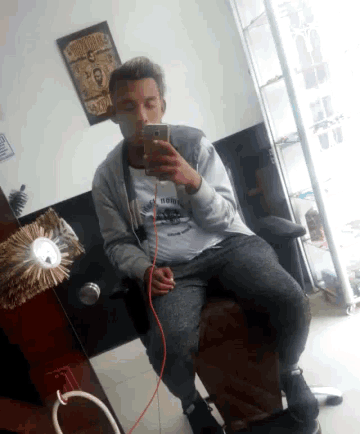 a man sitting in a chair taking a picture of himself with a picture of jesus on the wall behind him