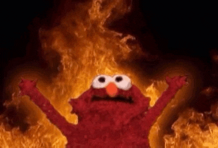 elmo from sesame street is standing in front of a burning fire .