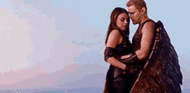 a man and a woman are standing next to each other and hugging . the man is wearing wings .