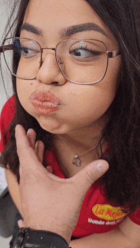 a woman wearing glasses and a red shirt that says la mejor makes a funny face