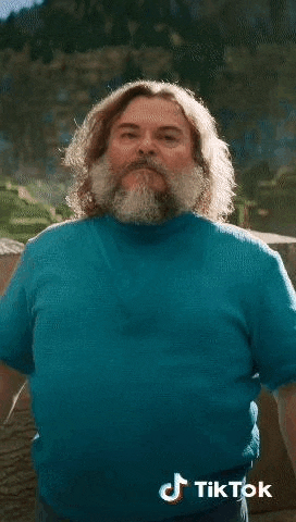 a man with a beard and long hair is wearing a blue sweater and standing in front of a mountain .