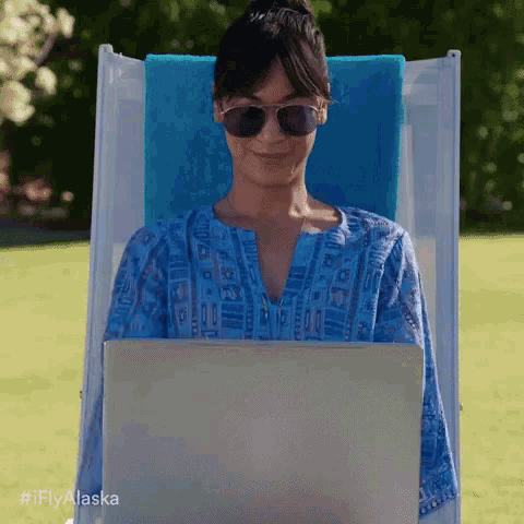a woman wearing sunglasses is sitting in a chair with a laptop on her lap .