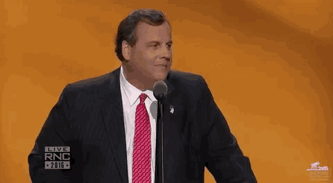 a man in a suit and tie is standing in front of a microphone on a stage .