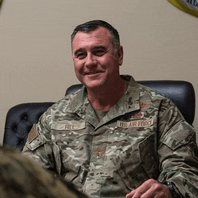 a man in a military uniform is sitting in a chair and smiling at the camera .