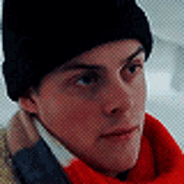 a man wearing a black hat and a red scarf is looking at the camera .