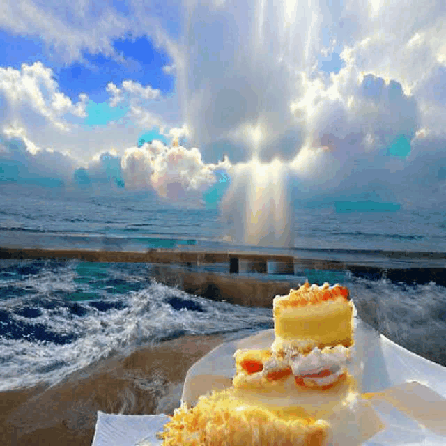 a piece of cake sits on a plate on the beach with the ocean in the background