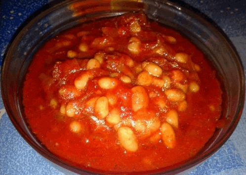 a bowl of baked beans with tomato sauce on a blue cloth