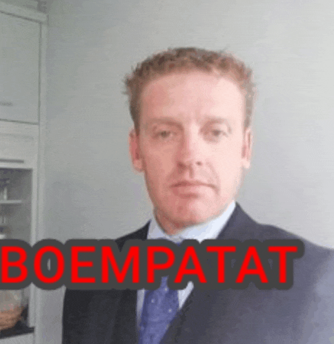 a man in a suit and tie is standing in front of a sign that says boempaat