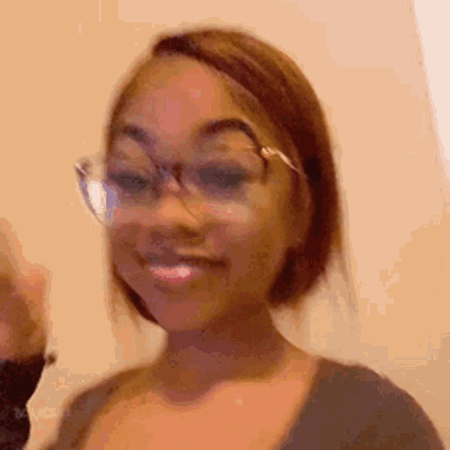 a woman wearing glasses and a gray shirt is smiling and waving .