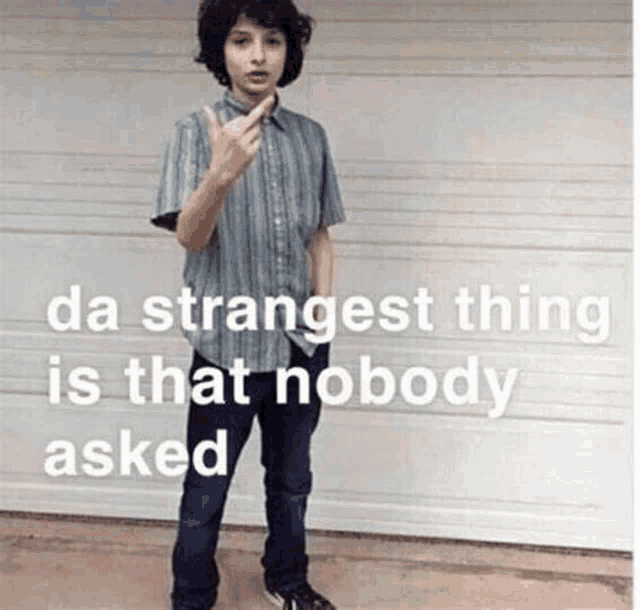 a young man is standing in front of a garage door giving the middle finger while wearing a striped shirt and jeans .